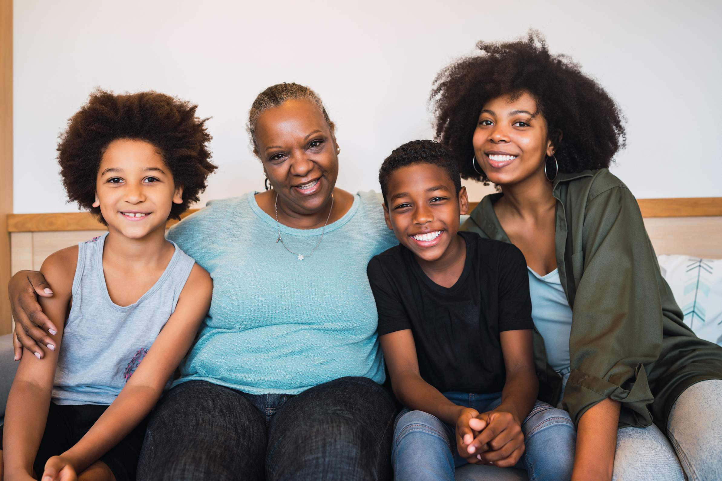 Portrait of African American grandmother, mother and children looking at camera and smiling while sitting on sofa at home. Family and lifestyle concept.